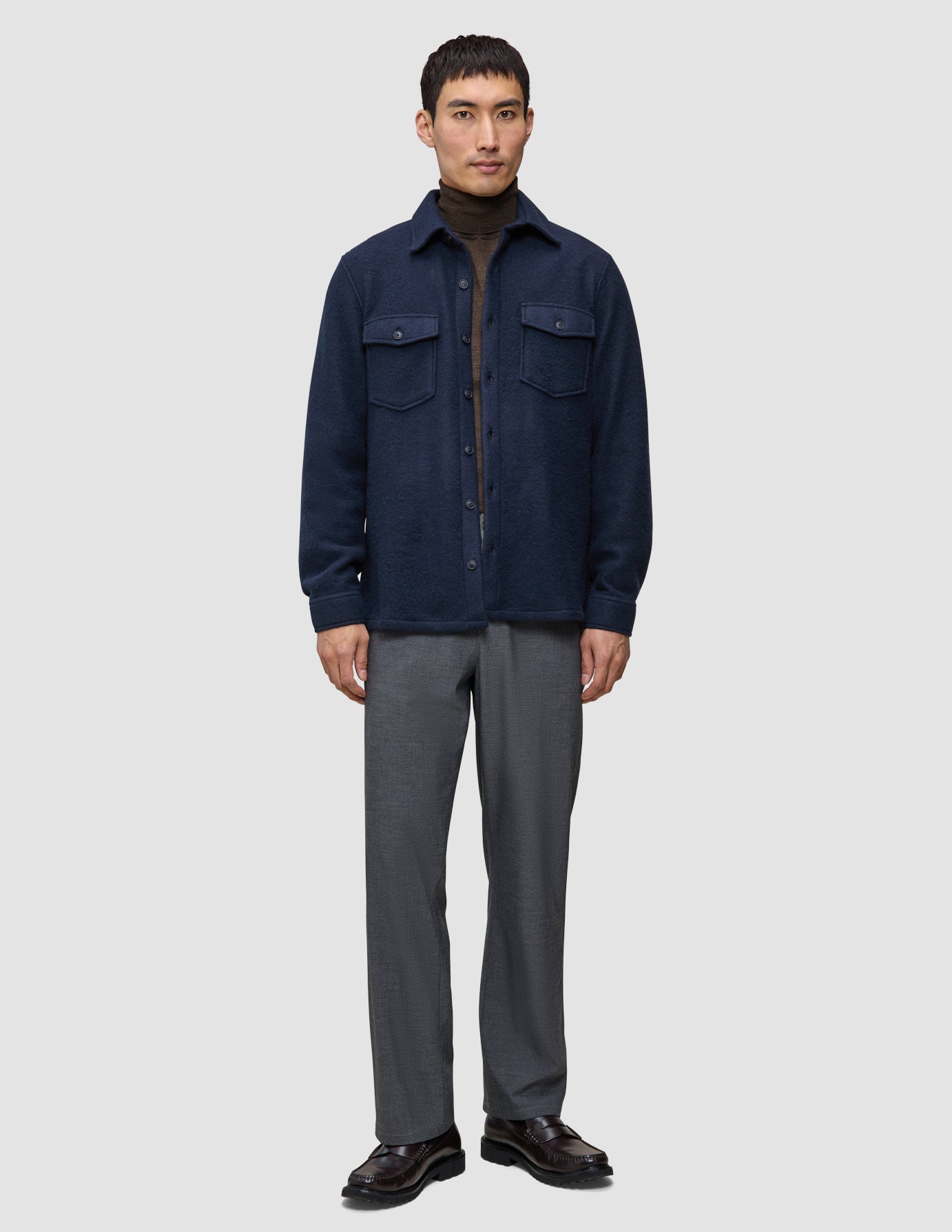 En mann i en dobbeltlags ullskjorte i mørk marineblå i regular-passform, brun turtleneck, grå bukser og loafers i skandinavisk stil.